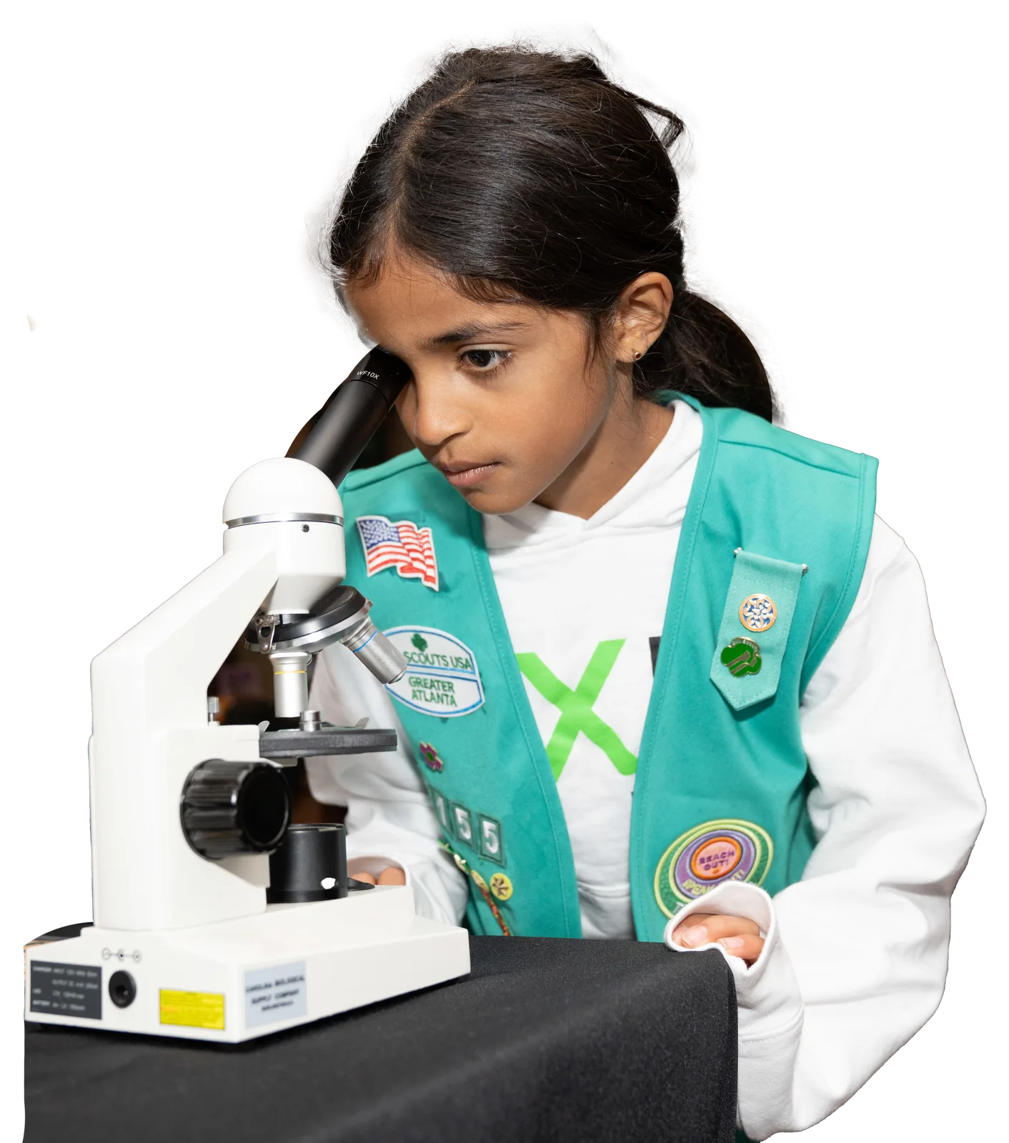 A Girl Scout in a teal vest looks into a microscope