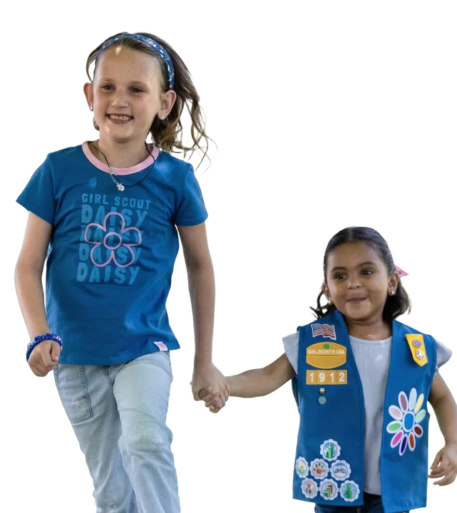 Two young Girl Scouts hold hands and run across a park